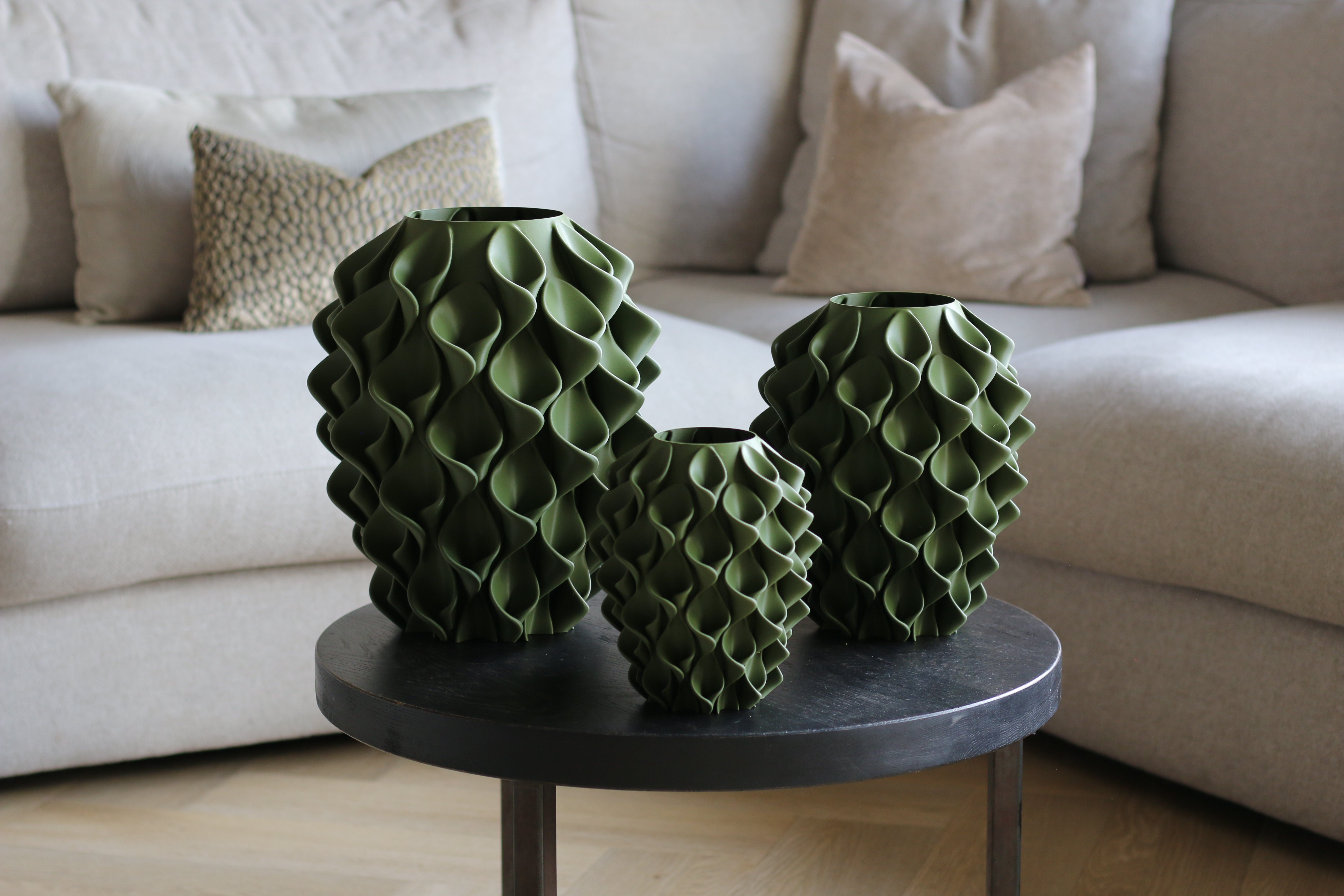 Drie olijfgroene coral vazen op een zwarte bijzettafel in een woonkamer – verschillende maten 3D-geprinte designvazen van Studio VormVezel