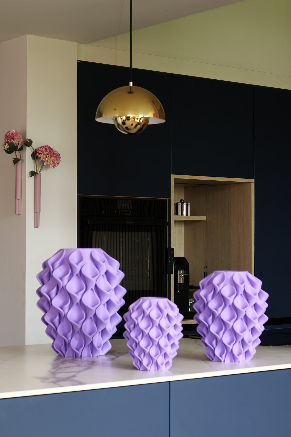 Drie Coral-vazen Lila in verschillende maten op een marmeren keukenblad voor een donkerblauwe keuken met messing hanglamp