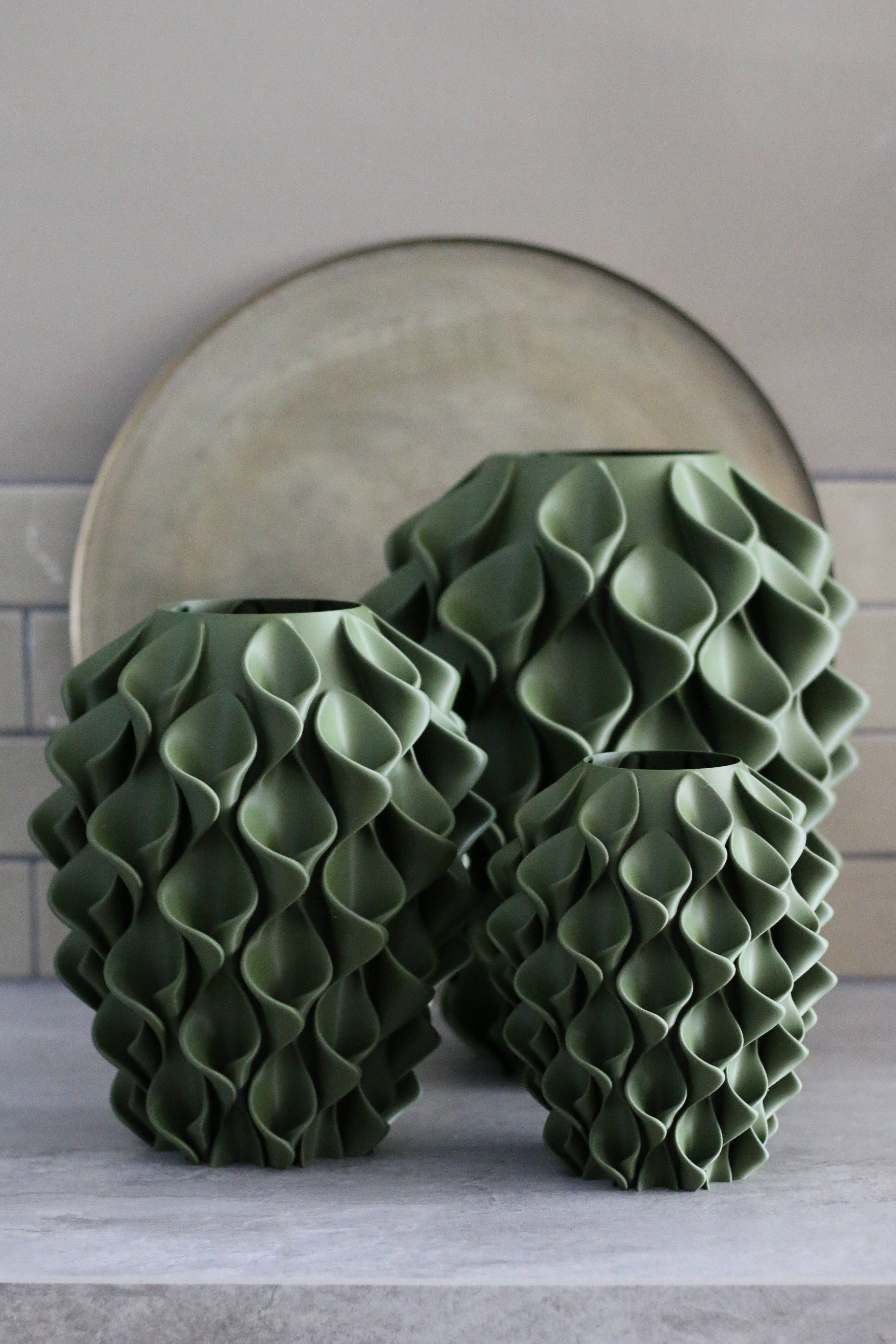 Twee olijfgroene coral vazen in verschillende maten op een stenen plank voor een ronde spiegel – handgemaakt 3D-geprint designobject van Studio VormVezel